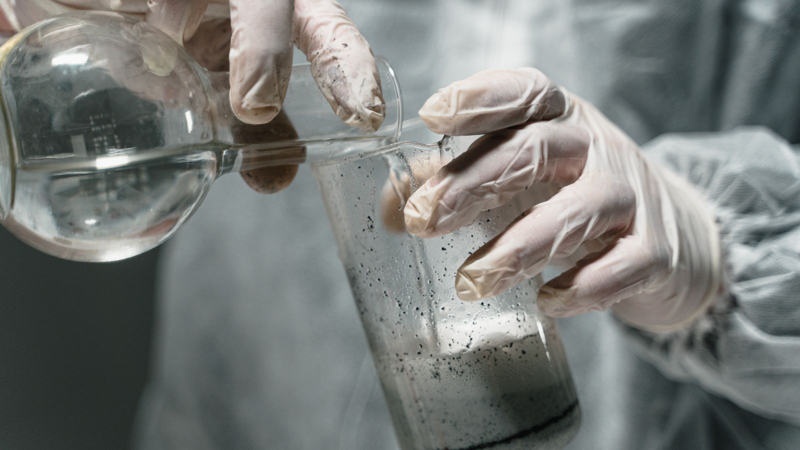 Close-up of scientist pouring liquid in laboratory experiment, wearing gloves.