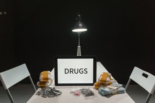 Free A dimly lit room with a sign displaying 'DRUGS' surrounded by money and illegal substances. Stock Photo