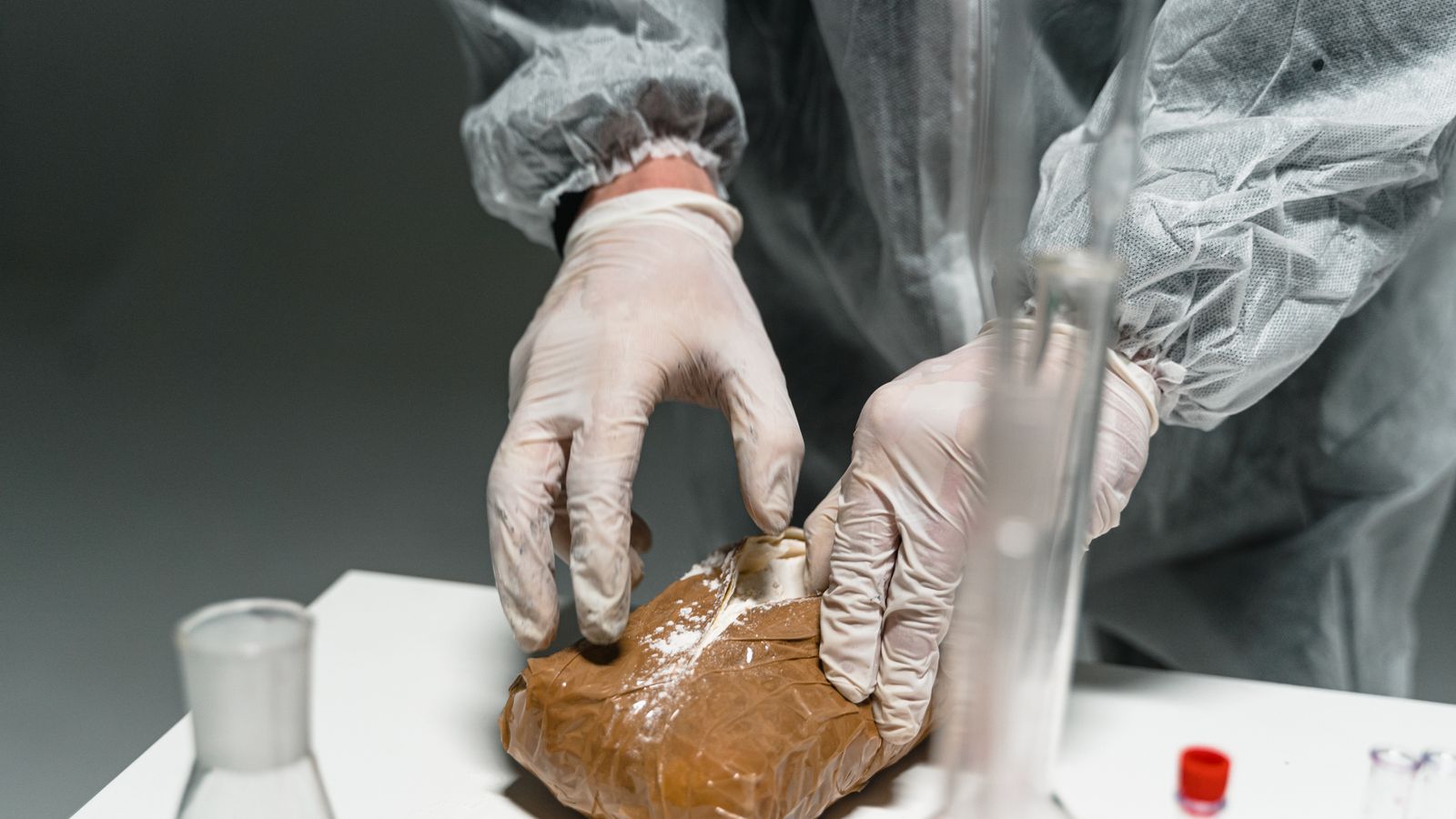 Lab worker analyzes powdered substance in a laboratory setting using safety gear.