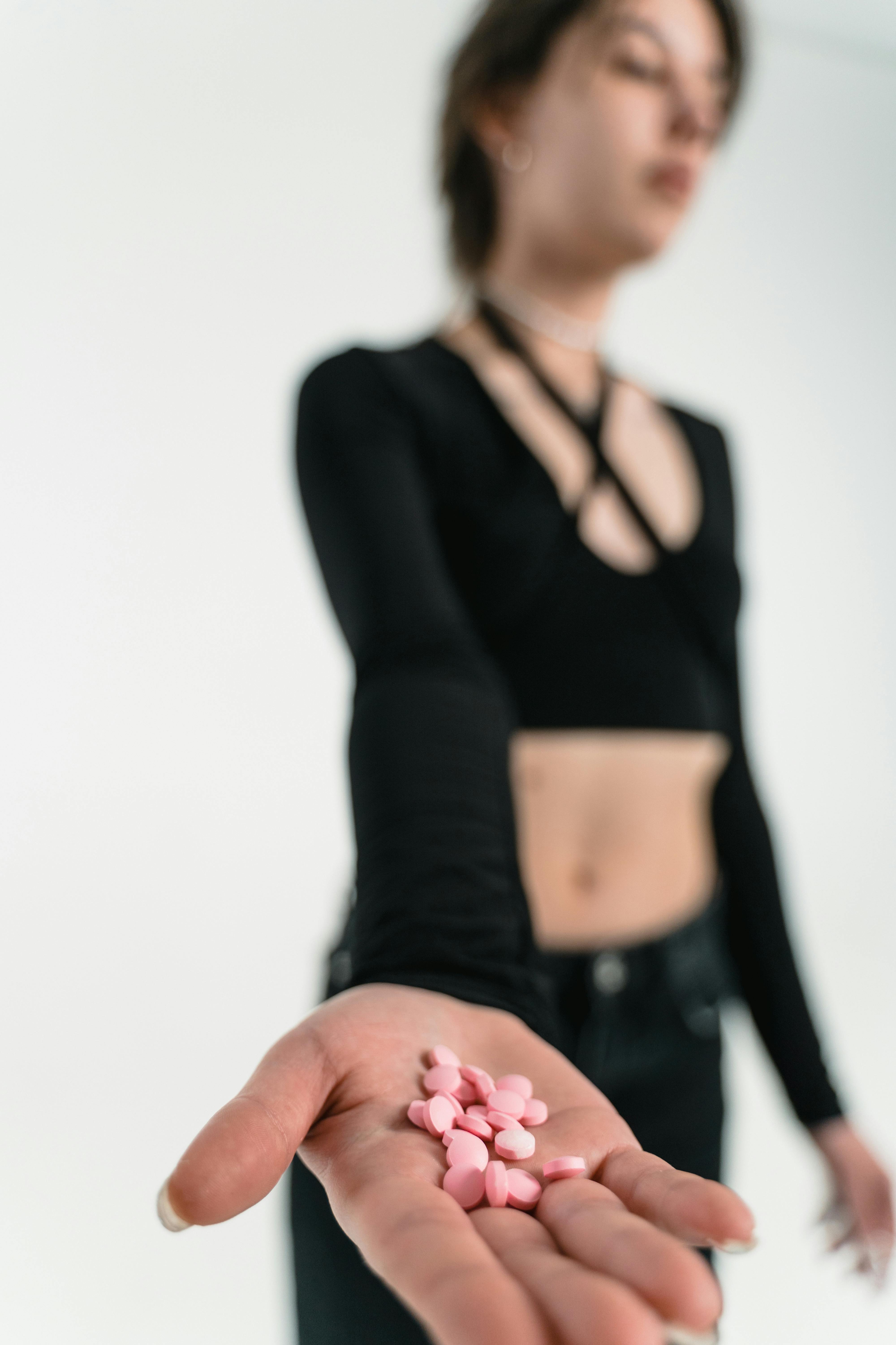 A conceptual photo of a woman in black offering pink pills with an extended hand.