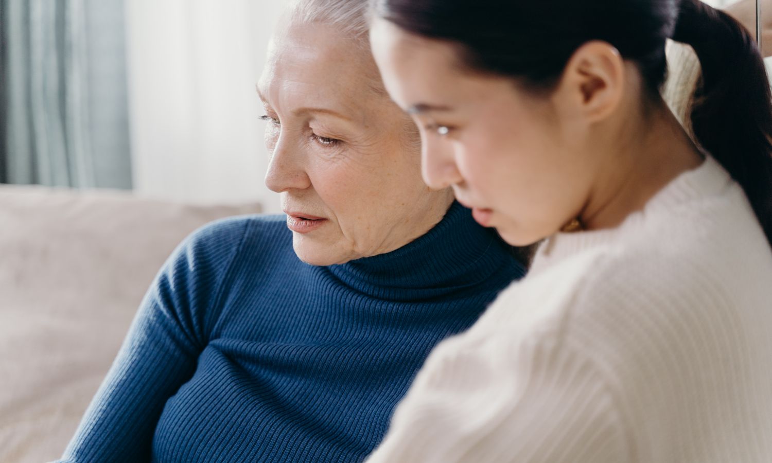 An older woman and her adult daughter talking together at home.