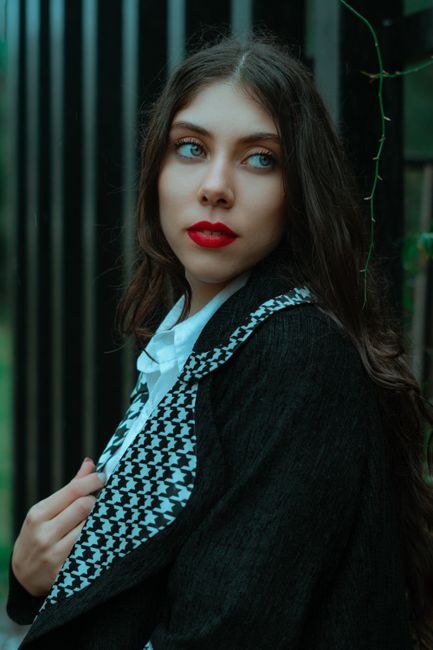 Side view of young female with long dark and red lips leaning on metal fence and looking away