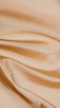 Close-up of smooth, beige silk fabric showcasing its soft and shiny texture.