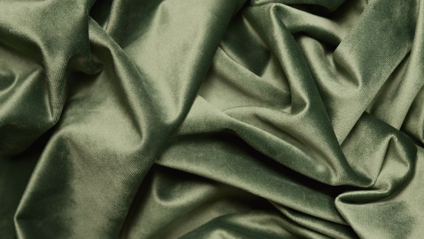 Close-up of an olive velvet cloth in soft folds, the pile catching the light along each crest.