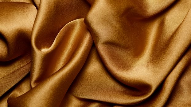 Close-up of smooth and shiny gold satin fabric with a wavy texture.