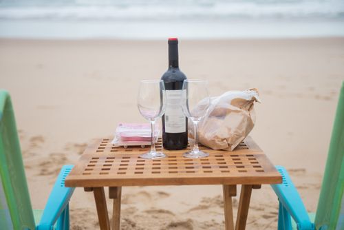 Free A serene beach picnic setup with wine and glasses on a wooden table by the shore in Portugal. Stock Photo