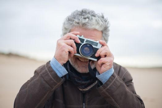 Senior man with white hair taking a photo with a vintage camera outdoors.