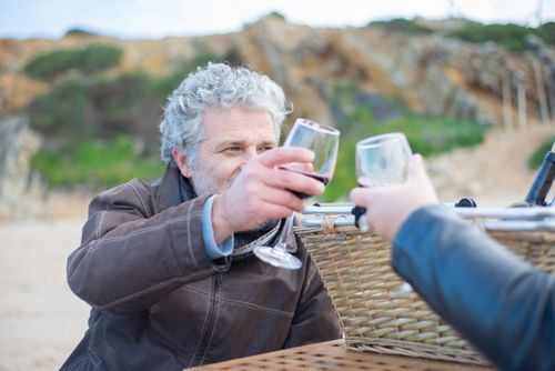 Free Senior man in brown jacket toasting wine during outdoor picnic with a basket in the serene Portuguese countryside. Stock Photo