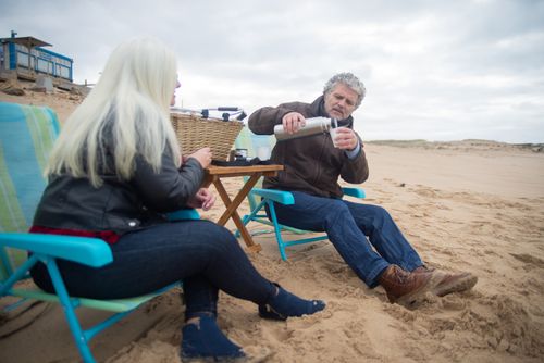 Free Senior couple relaxing on a sandy beach in Portugal, enjoying a drink together. Stock Photo