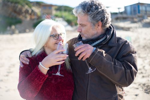 Free Happy senior couple sharing wine on a sandy beach in Portugal. Stock Photo