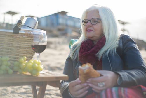 Free Senior woman having a beach picnic in Portugal with wine, baguette, and grapes. Stock Photo