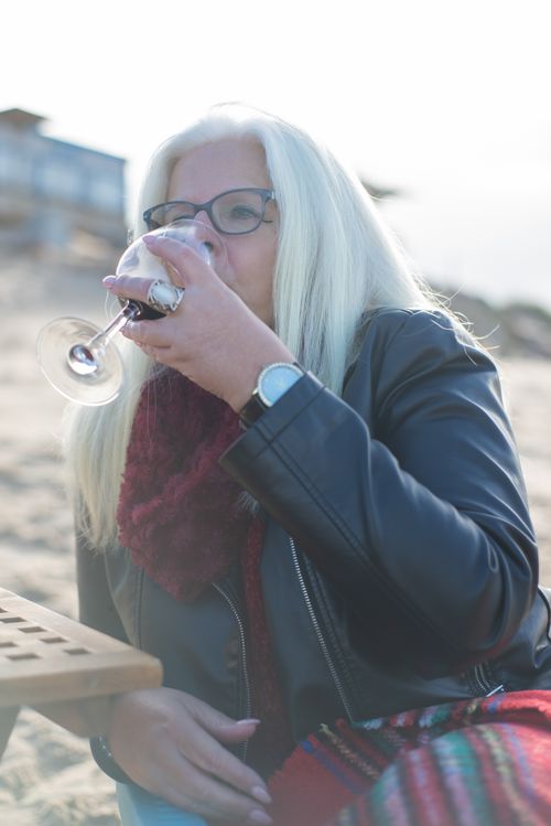 Free Elderly woman in a leather jacket enjoying wine on a sunny Portuguese beach. Stock Photo