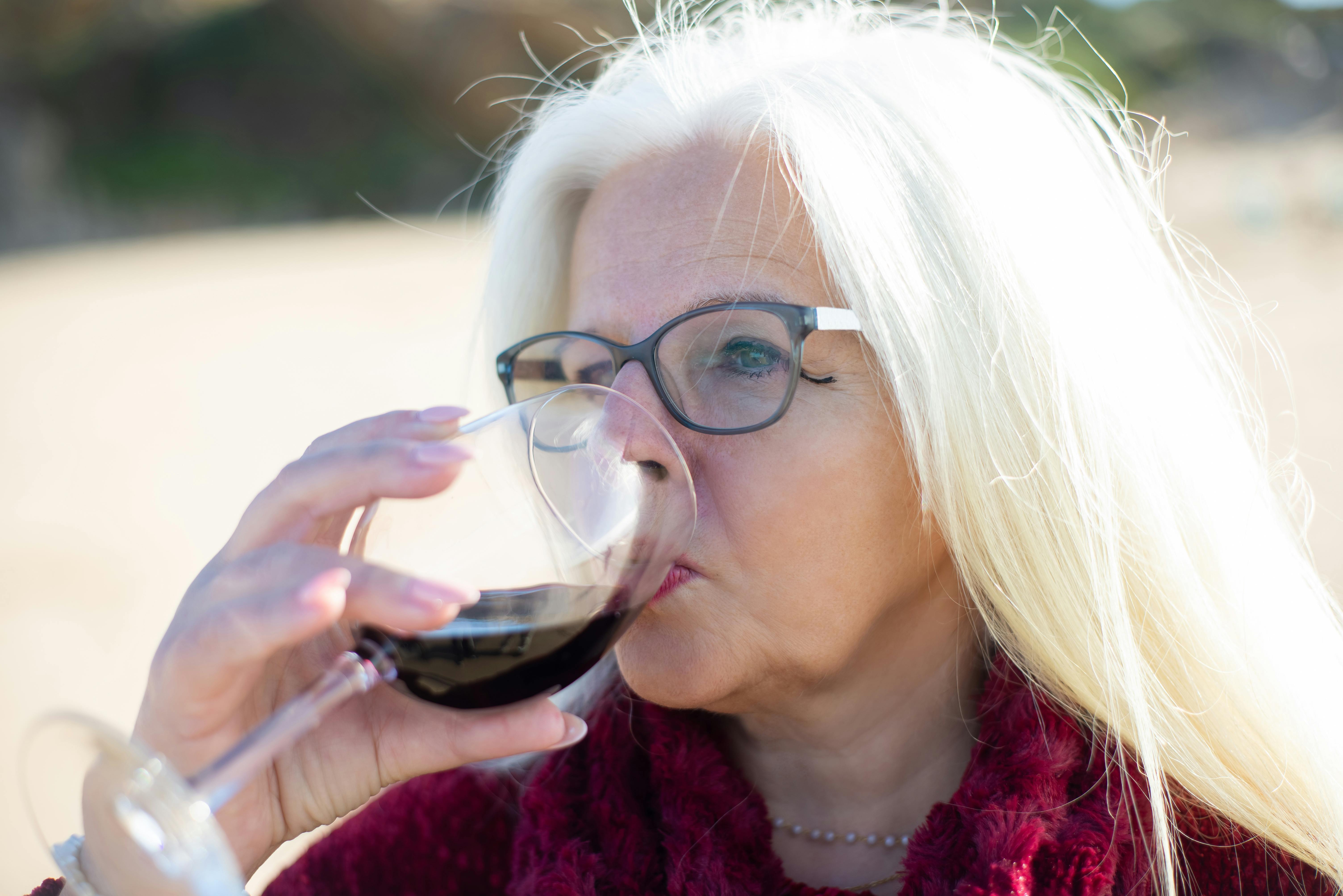 Senior woman with white hair and glasses drinking red wine on a sunny day in Portugal.