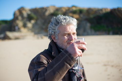 Free Senior man with gray hair savoring wine outdoors on a sunny Portuguese beach. Stock Photo