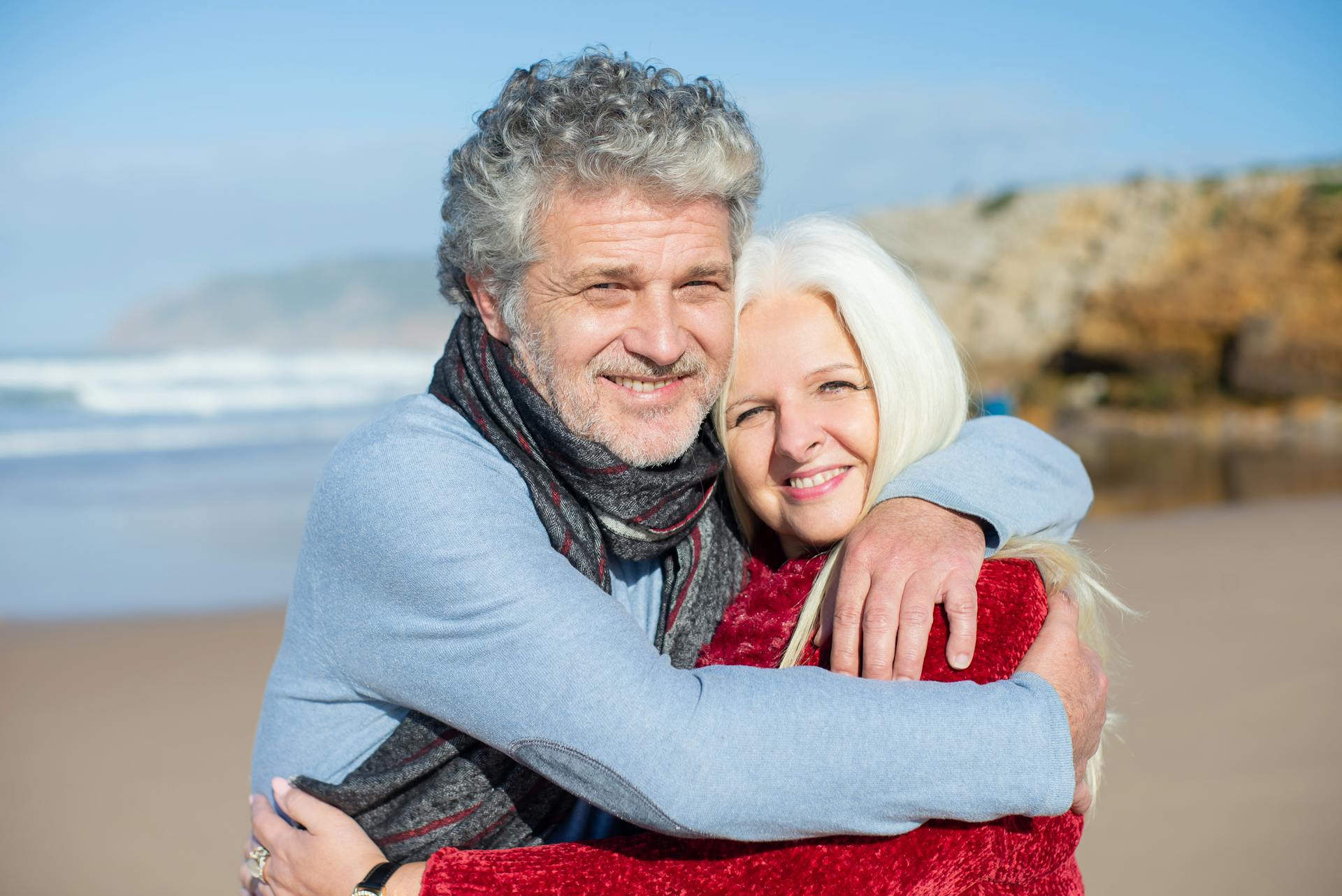 Joyful elderly couple hugging on a sunny beach in Portugal, enjoying a romantic day.