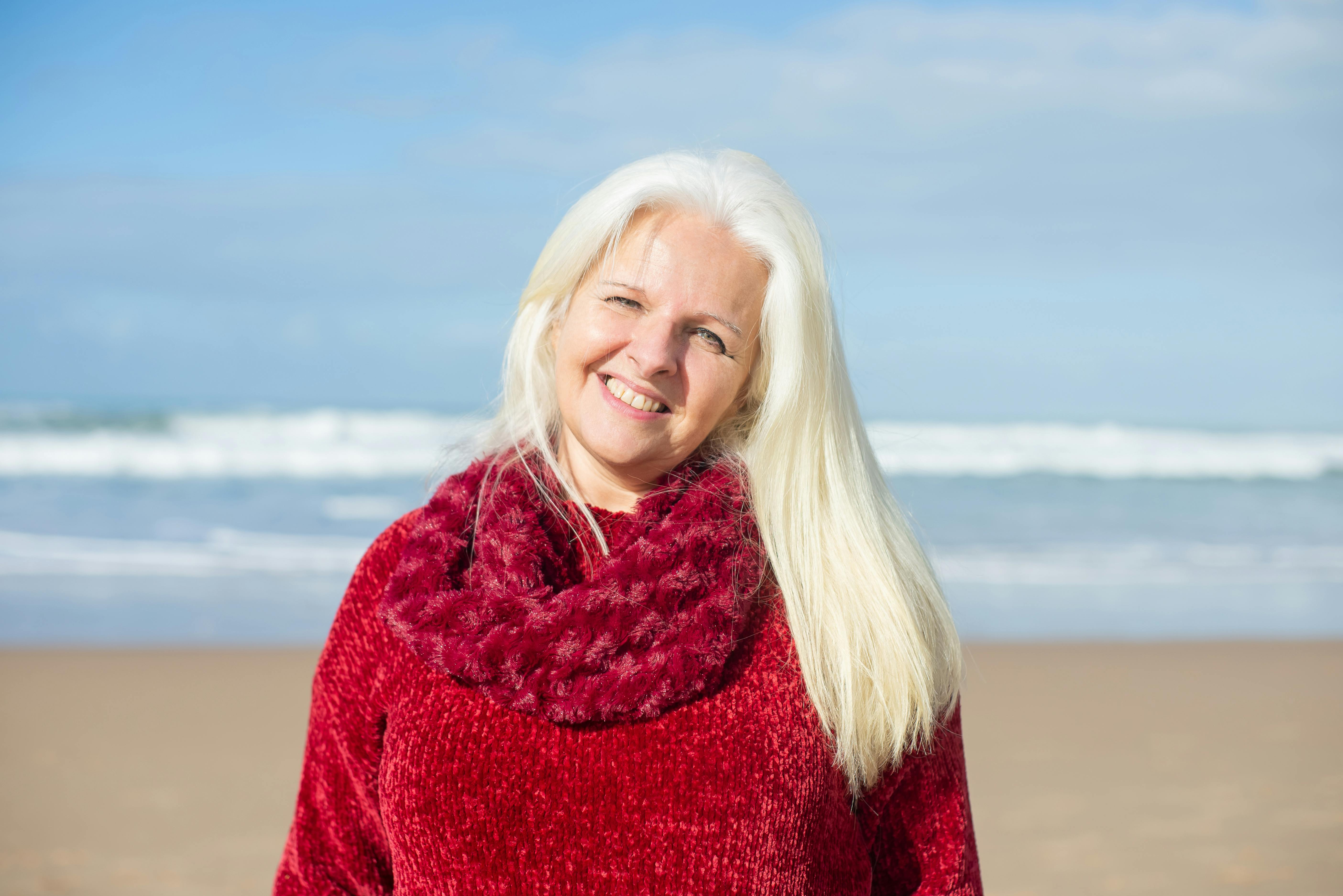Senior woman in red sweater smiling at the beach in Portugal, a perfect blend of happiness and scenic ocean view.