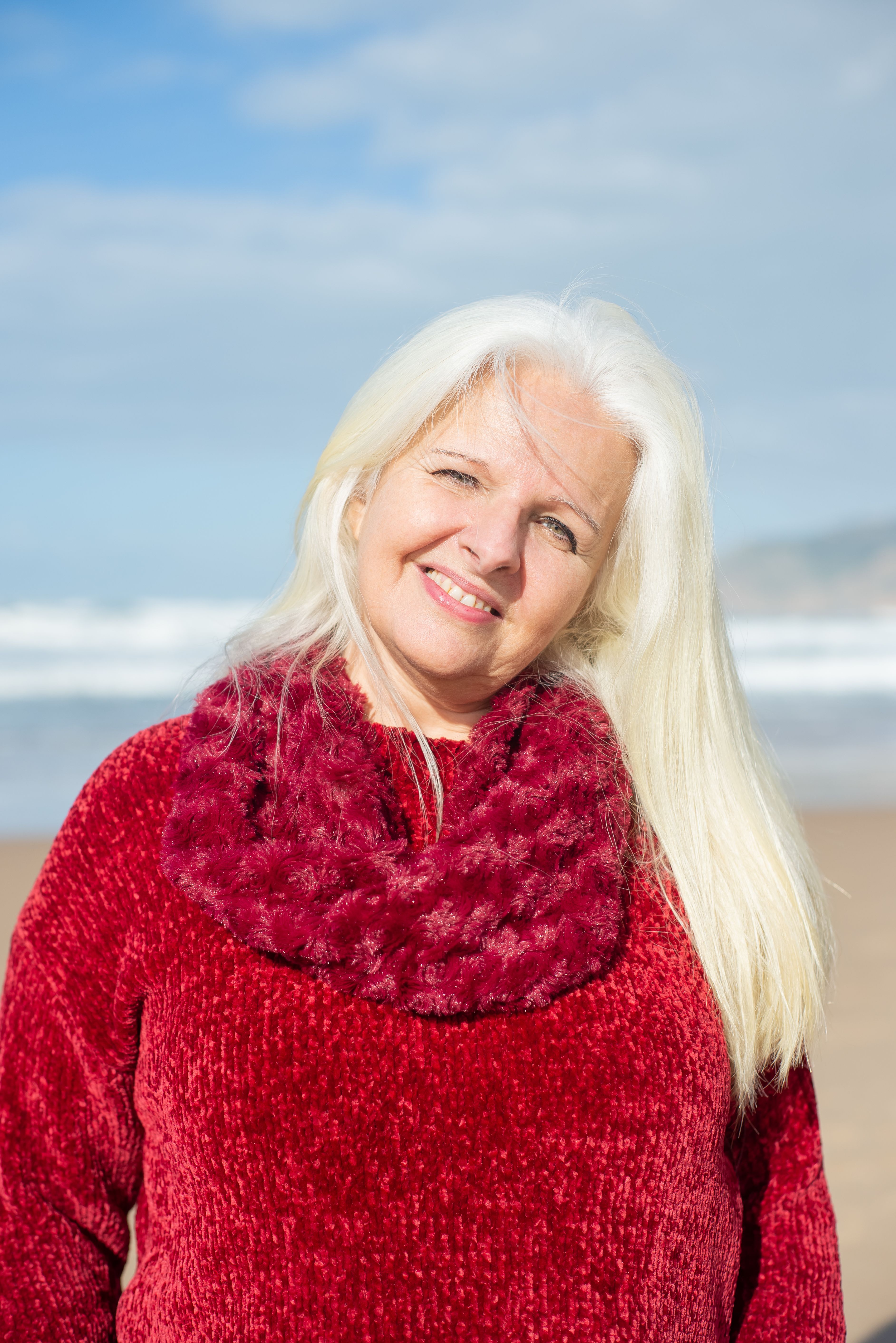Elderly woman in red sweater smiling on a sunny beach in Portugal.
