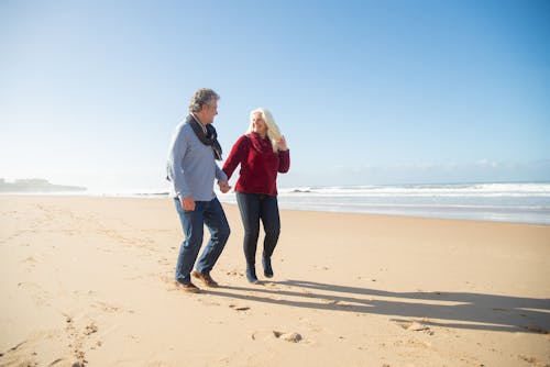 Free A Couple Holding Hands While Walking on the Shore Stock Photo