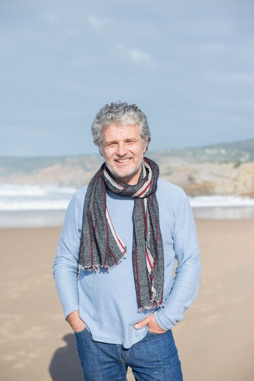 Free Happy elderly man with gray hair standing on a sunny beach, wearing a scarf and sweater. Stock Photo