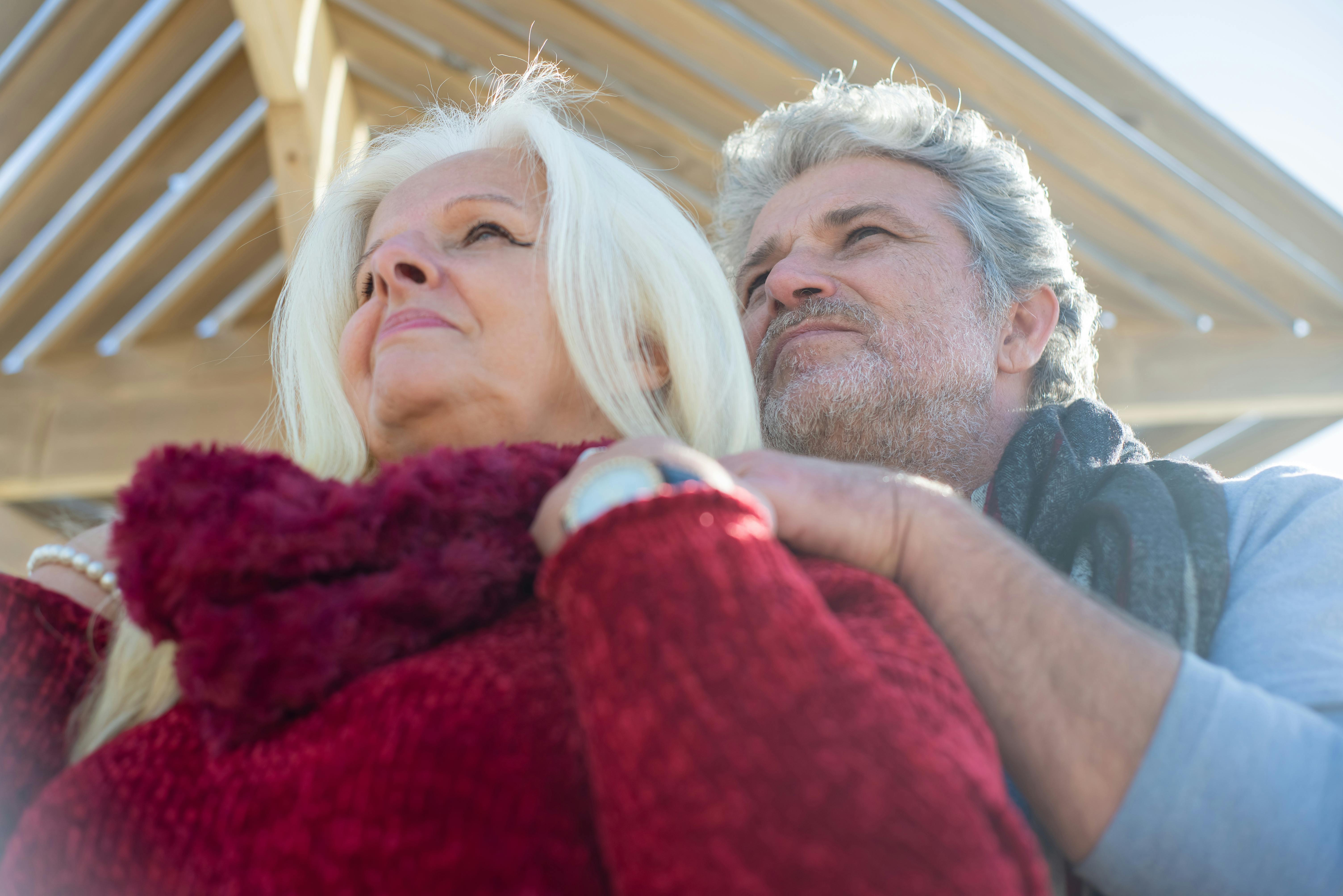 Loving senior couple embracing outdoors, under wooden structure in sunny Portugal.