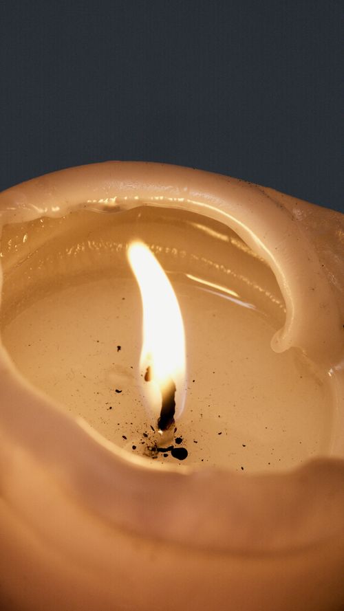 Free Close-up view of a lit candle with wax drips and a glowing flame against a dark background. Stock Photo
