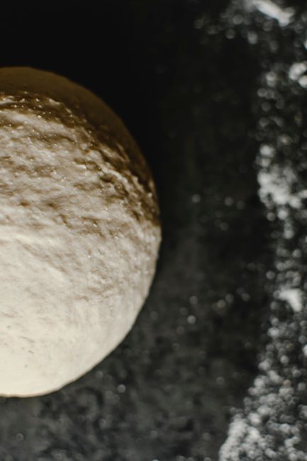 A round of stretched pizza dough dusted with flour, showing air bubbles along the puffy edge before topping.