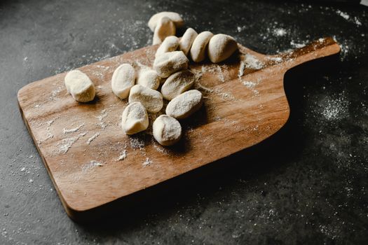 Flour-dusted homemade dough pieces on a wooden chopping board, ready for cooking.