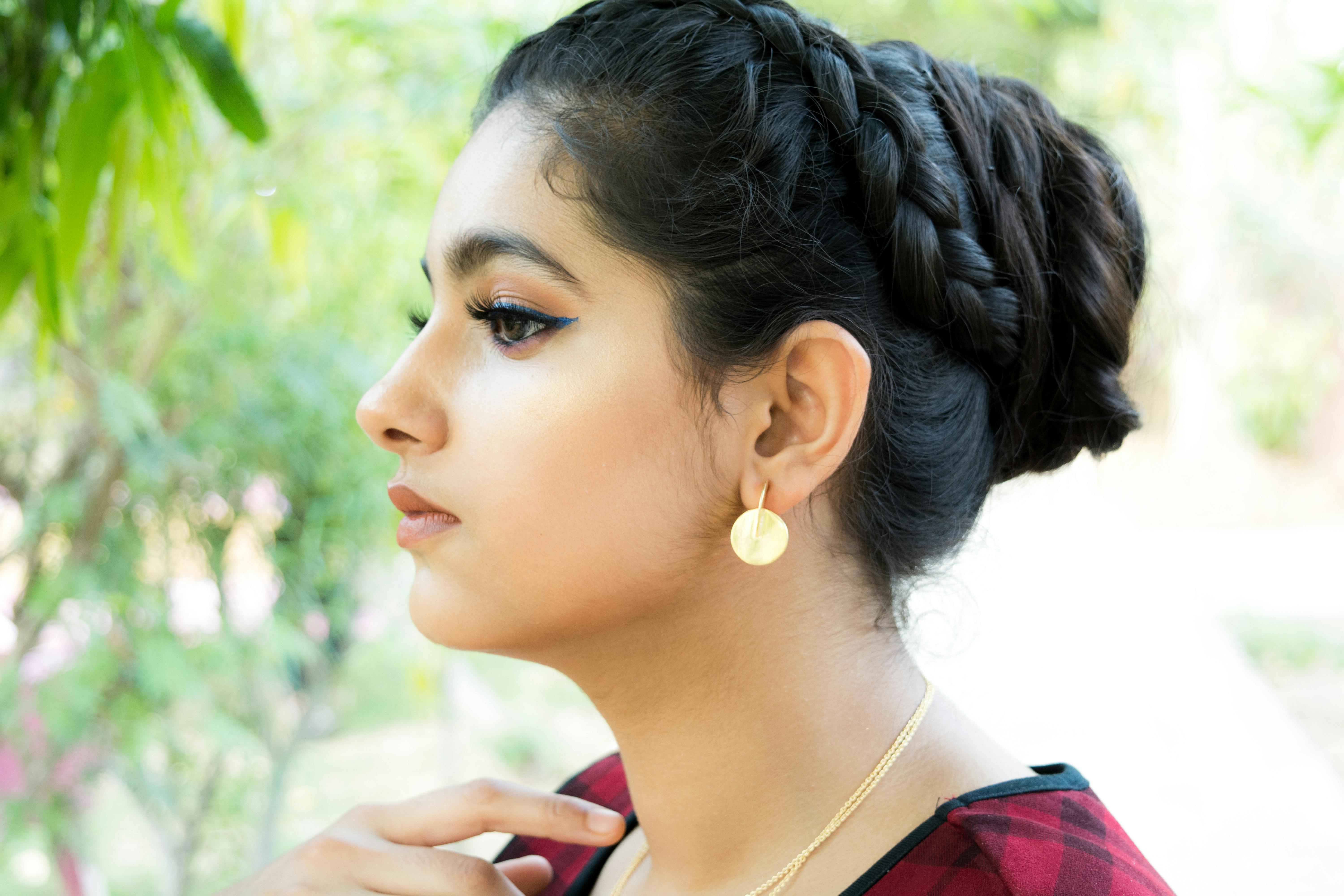 Elegant side profile portrait of a young woman wearing stylish jewelry with a braided hairstyle.
