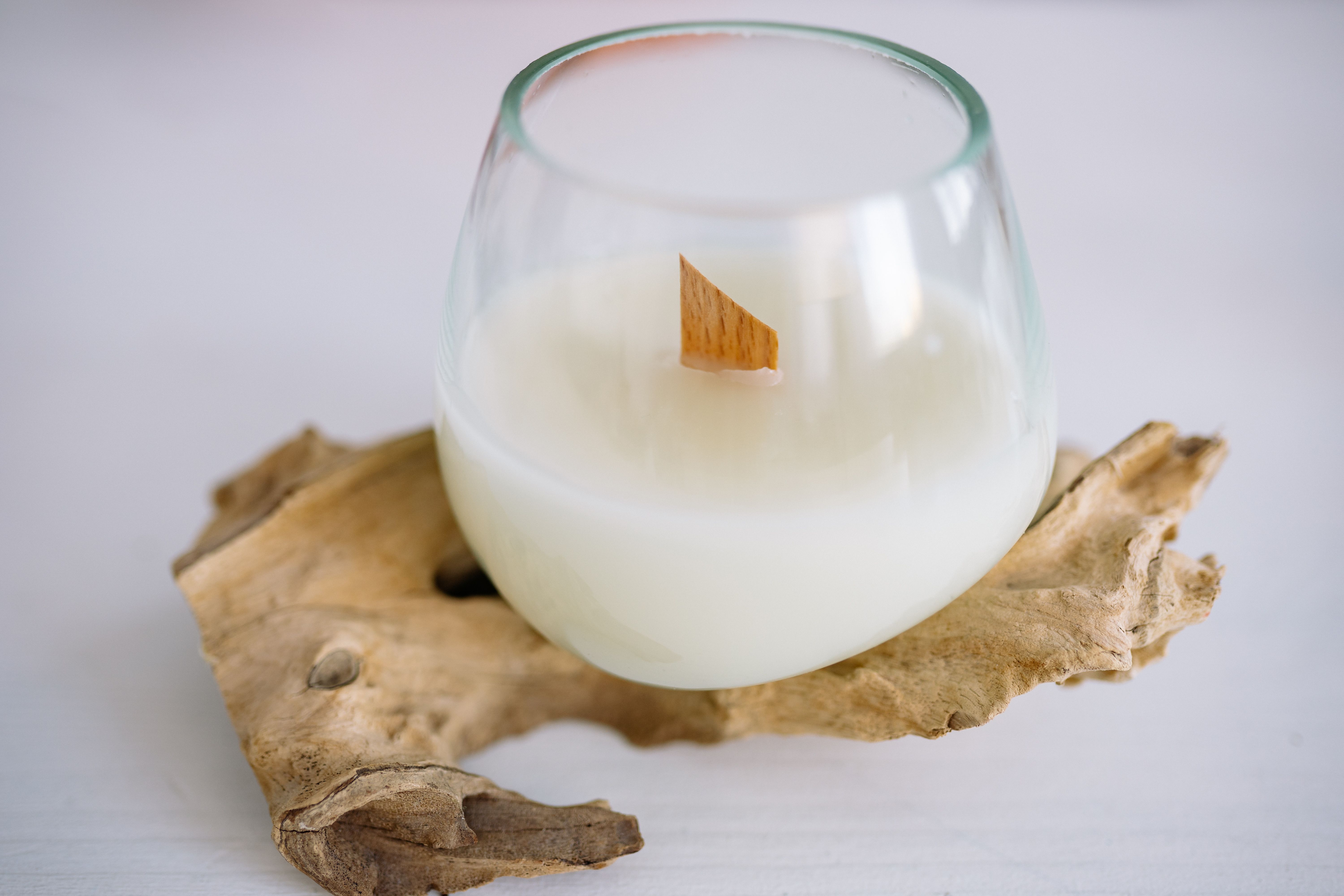 A minimalist glass candle with a wooden wick on driftwood. Ideal for modern decor enthusiasts.