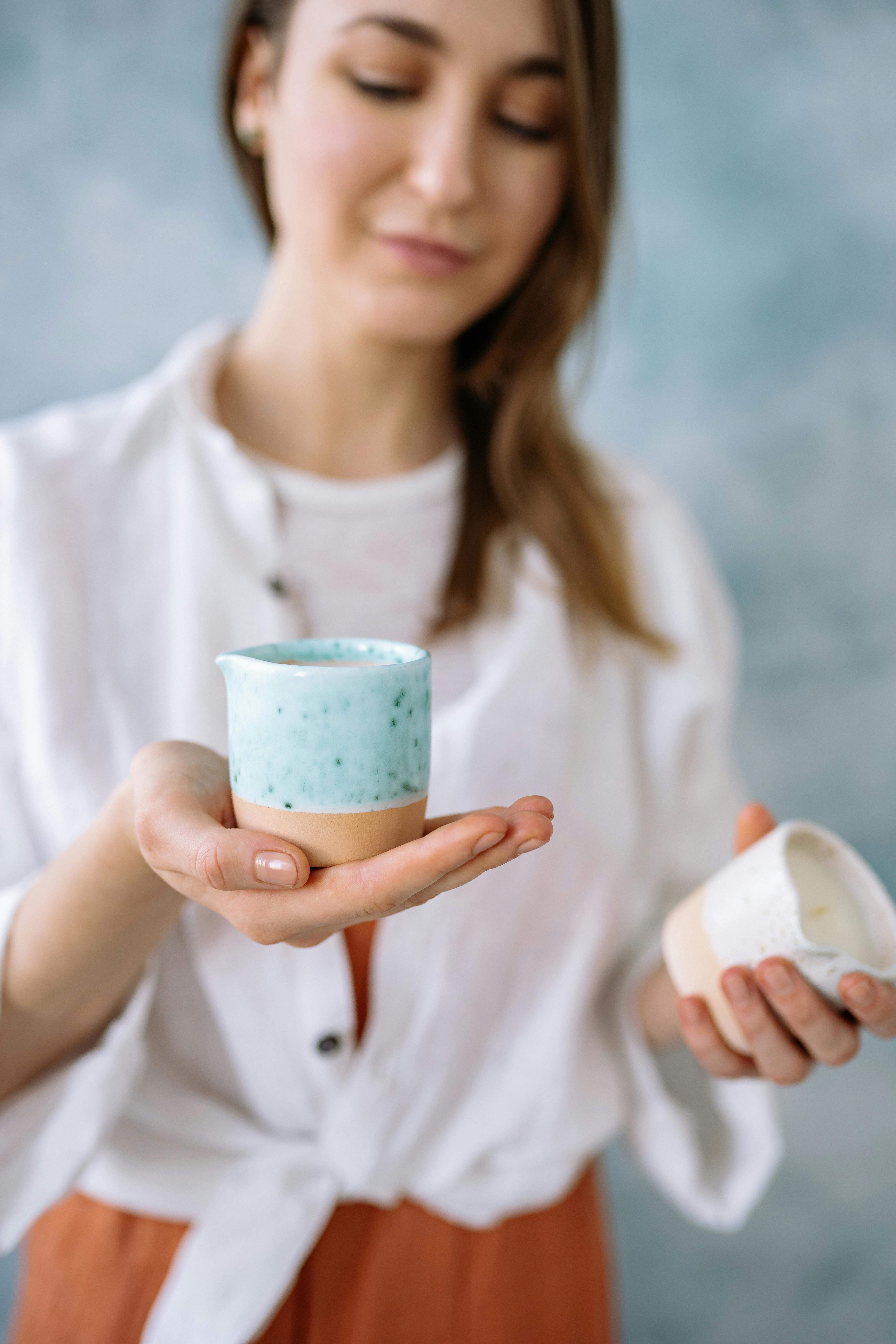 A woman displays handmade ceramic candle cups, highlighting their unique texture and color.
