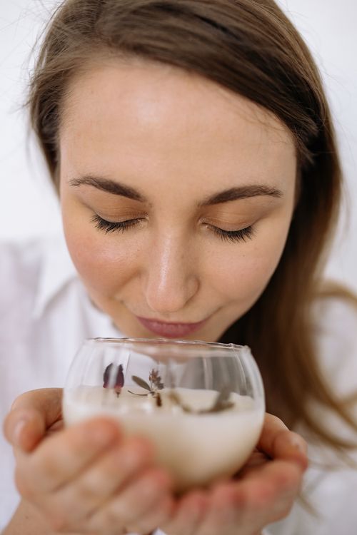 Free Close-up of a woman savoring the scent of a lit candle, eyes closed in relaxation. Stock Photo