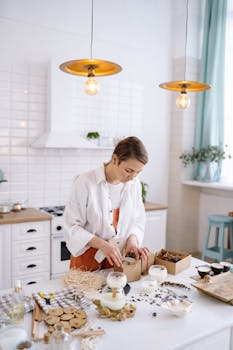 A woman carefully crafts handmade candles in a modern, bright kitchen setting. Ideal for DIY or craft enthusiasts.