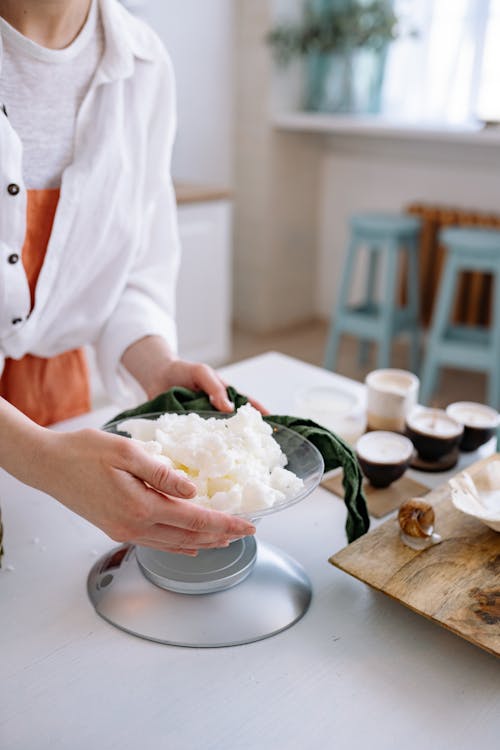 Person in White Long Sleeve Weighing the Candle Wax