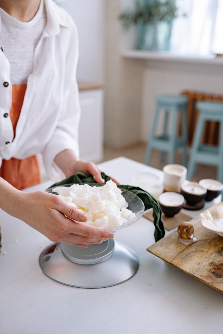 Person In White Long Sleeve Weighing The Candle Wax