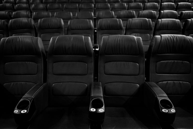 Grayscale image of empty leather cinema seats in a neat row.