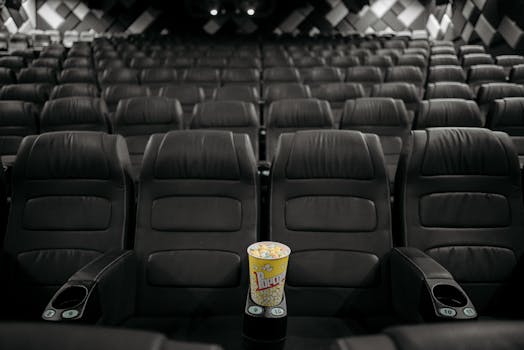 An empty cinema hall with black leather seats and a bucket of popcorn on an armrest.
