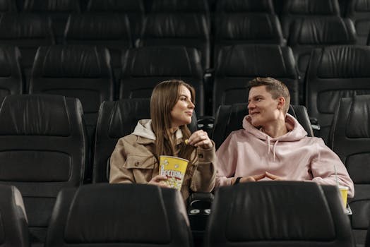 A couple sits in an empty cinema, enjoying popcorn and conversation in a cozy setting.