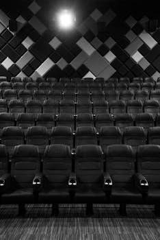 An empty grayscale movie theater showcasing leather seats and a geometric wall design.