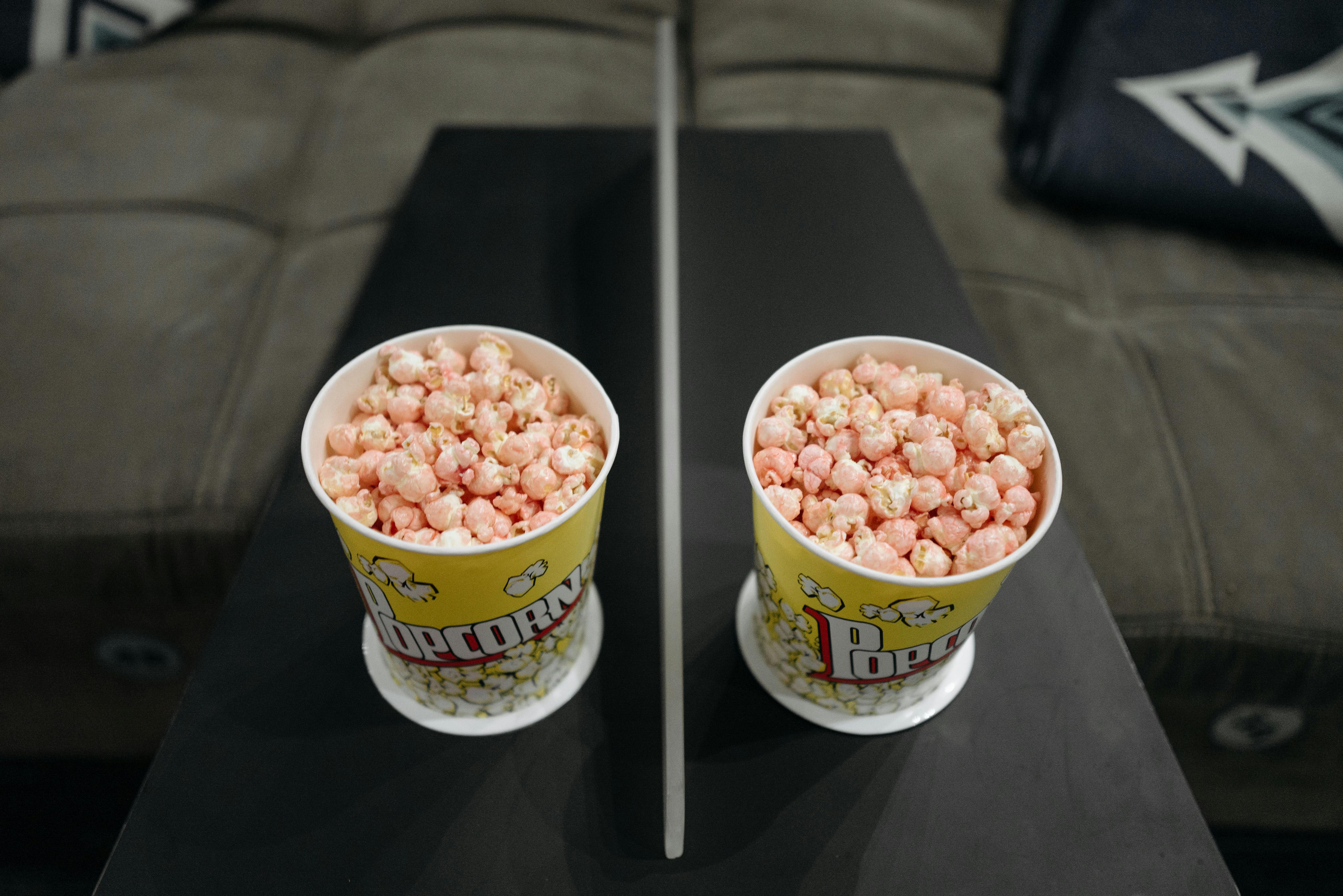 Two buckets of pink popcorn placed on a sofa armrest, offering a cozy movie night setup.