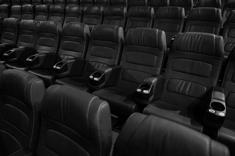 Black and white image of empty leather seats in an indoor movie theater.