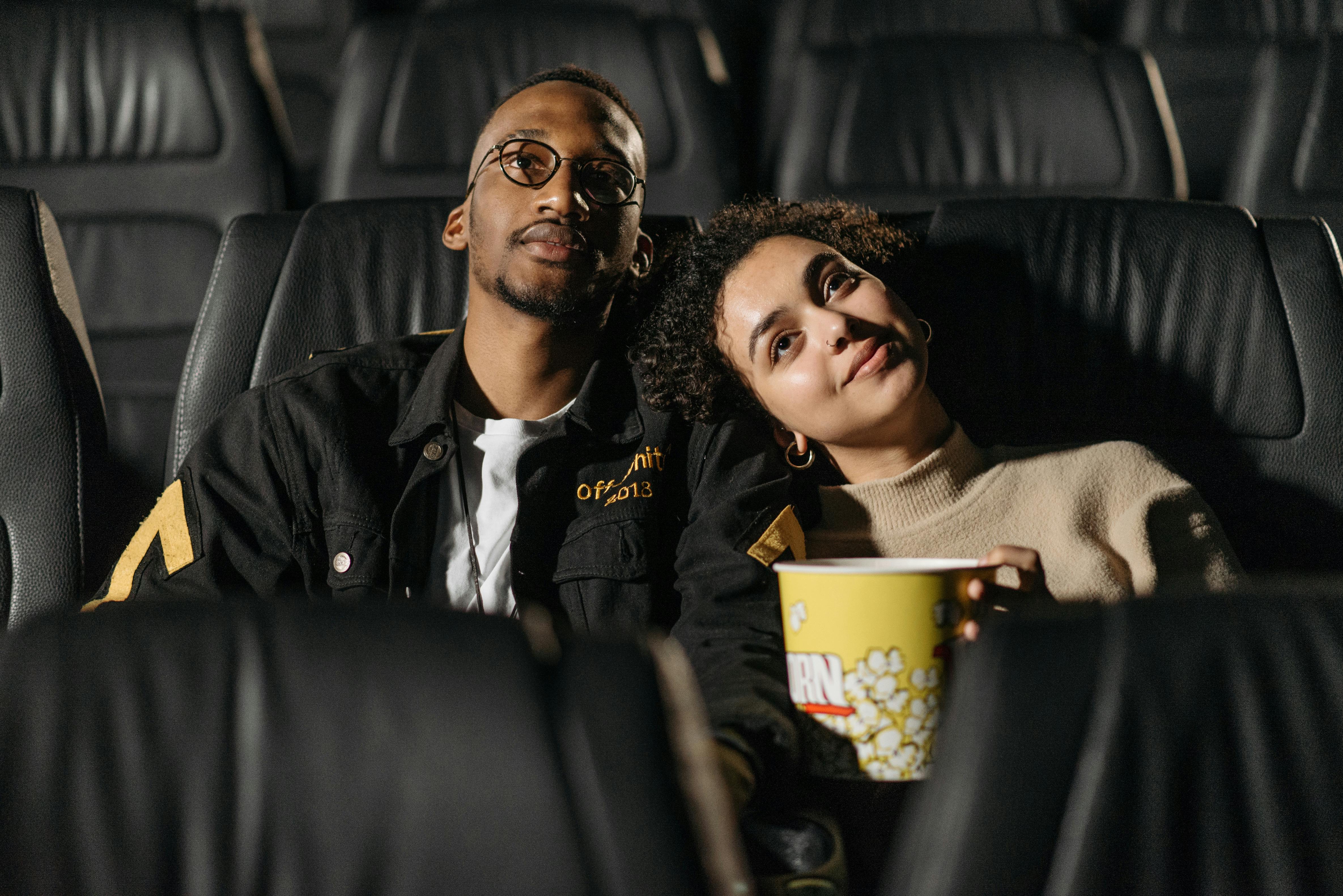 A couple enjoying a movie date, sitting closely in a theater, sharing popcorn.