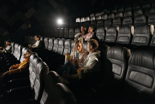 Free Couple sharing popcorn in a dimly lit movie theater with other viewers scattered. Stock Photo