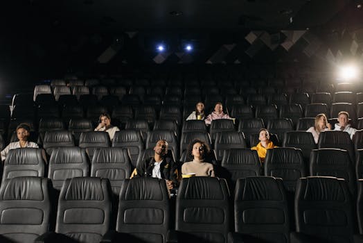 Image of diverse audience sparsely seated in a dimly lit cinema hall.