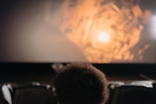 A person with afro hair sits in a theater, watching a movie on a large screen.