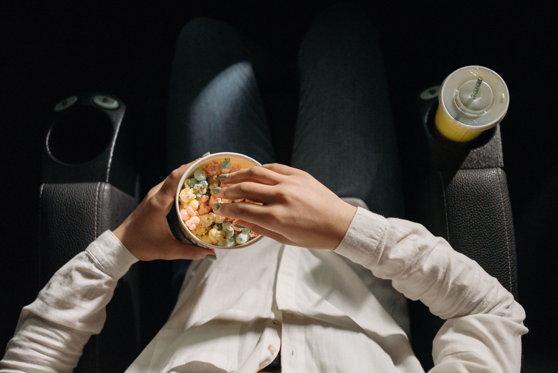 Close-up of a person holding colorful popcorn in a cinema seat.