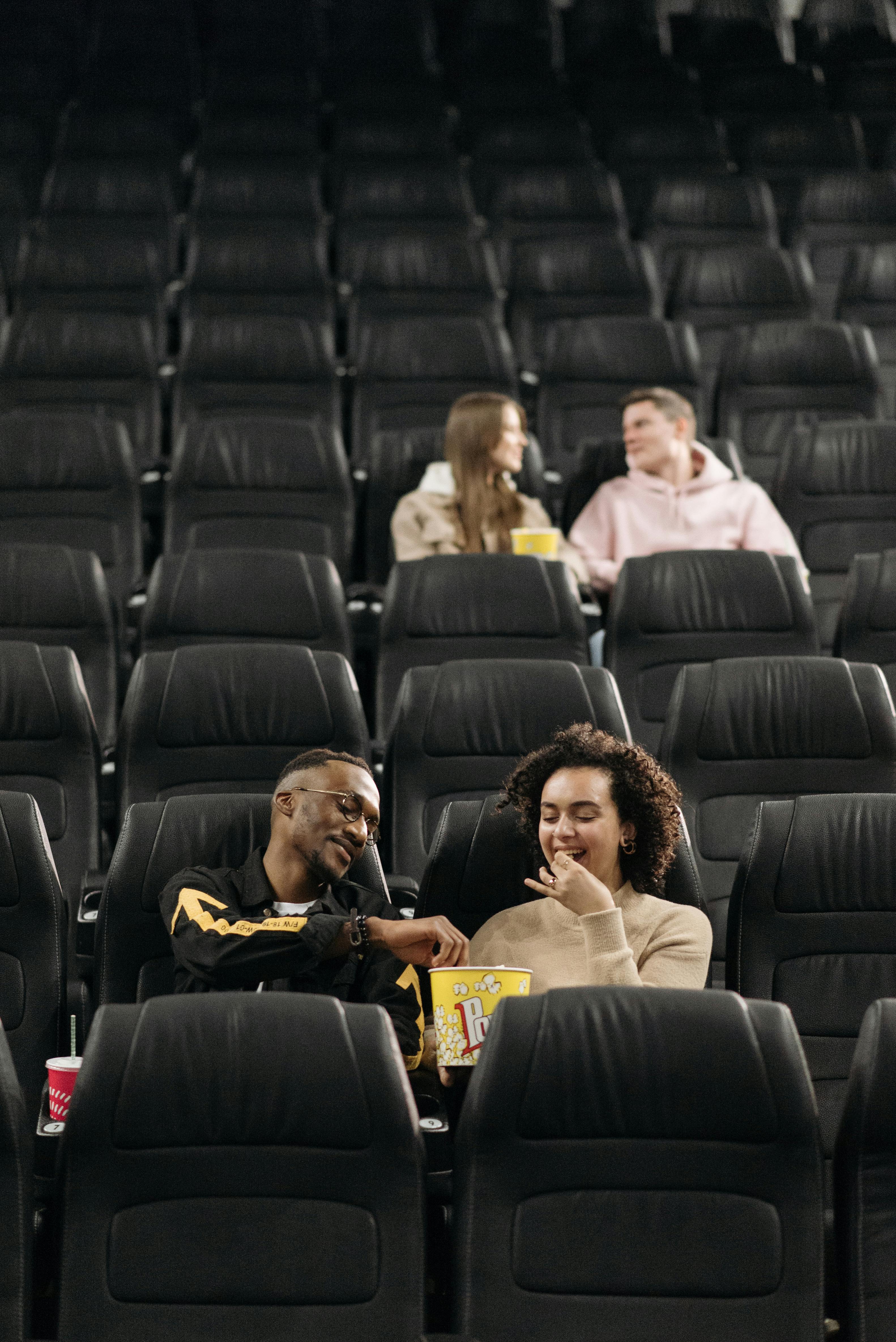 Free Two couples enjoying popcorn while watching a movie in an empty cinema. Stock Photo