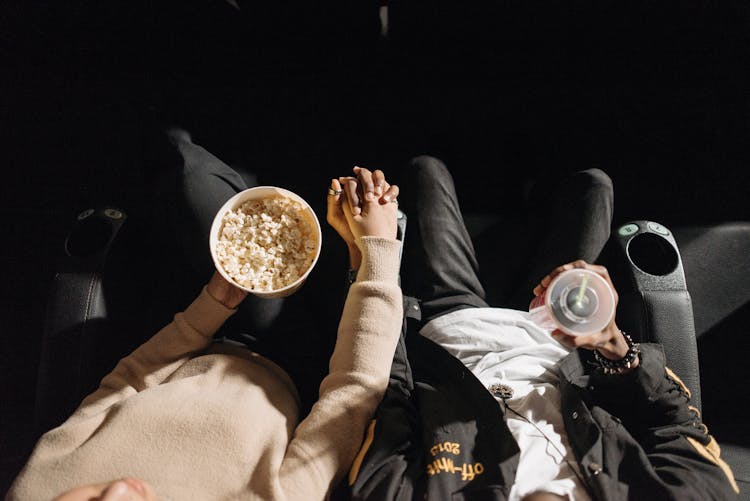 A Couple With Popcorn And Drinks Holding Hands