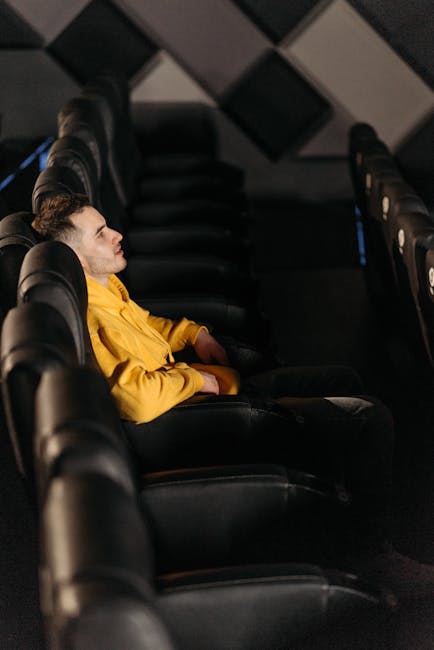 A young man in a yellow jacket relaxes in an empty cinema, enjoying solitude.