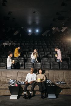 A couple sitting in an empty theater holding popcorn, enjoying a movie night indoors.