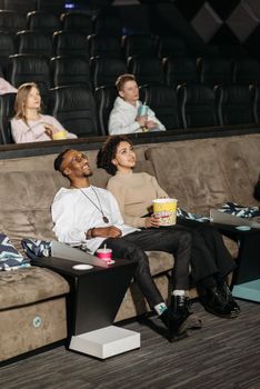 Couple sitting and smiling while watching a movie in a comfortable theater setting.